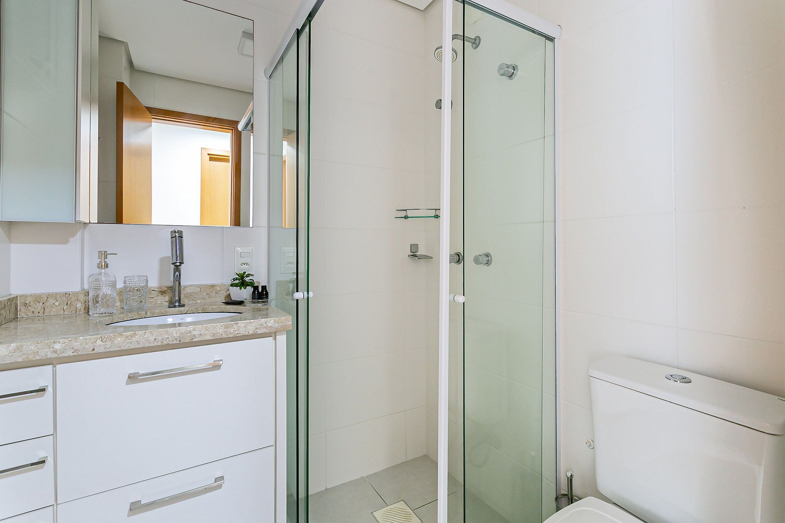 Une salle de bain moderne avec une douche à parois de verre, un lavabo doté d’un plan de toilette en marbre et des toilettes.