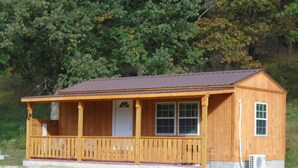 Une cabane en bois avec une véranda, une porte et des fenêtres.