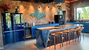 A modern kitchen with a central island, bar stools, and a large window with a view of cacti.