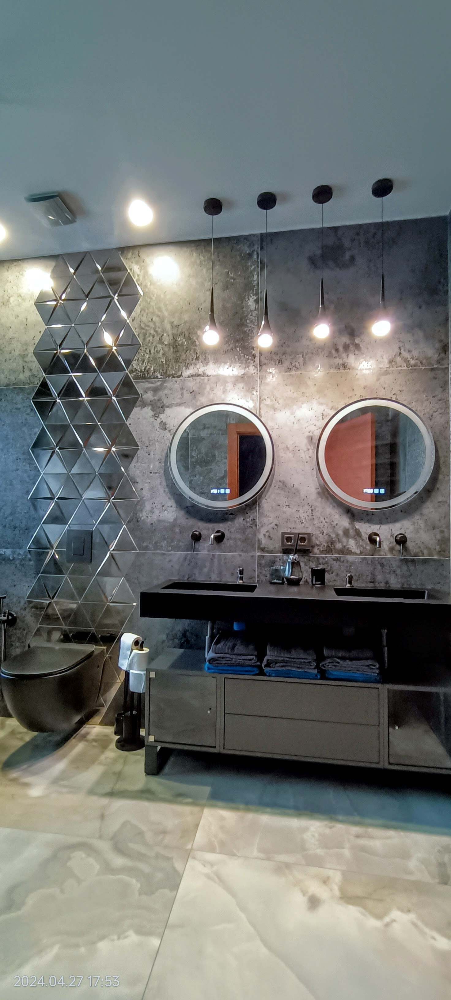 Et moderne badeværelse med et dobbeltvaskarrangement, en geometrisk vægdekoration og et toilet.