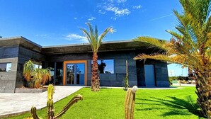 A modern house with a flat roof, large windows, and a well-maintained lawn with cacti.