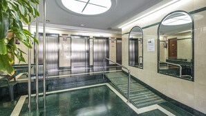 Hotellin aula, jossa on keskeisellä paikalla sijaitseva portaikko, hissit ja suuri peili, joka heijastaa tilaa.