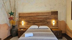 Un dormitorio con cabecera de madera, dos mesitas de noche, una cama con ropa de cama a rayas y un jarrón con adornos decorativos.