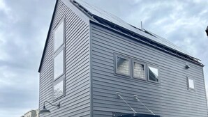 A two-story building with a dark exterior, a garage door, and a small front yard with a brick pathway. - Walkable Studio in Downtown Bar Harbor [Sea Smoke] (Bar Harbor)