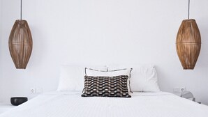 Uma cama bem arrumada com almofada estampada, duas luminárias fixadas na parede e uma tigela preta na lateral.