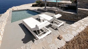 Área de piscina com espreguiçadeiras e um muro de pedra com vista para o mar.