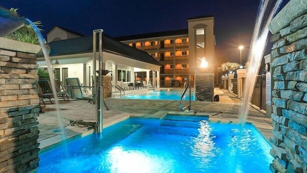 A swimming pool with a waterfall feature, surrounded by stone walls and lounge chairs. - Pool, Splash Pad & Hot Tub, Private Balcony, Close to Beach (Miramar Beach)