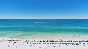 Une plage bordée de rangées de parasols bleus et de sable blanc.