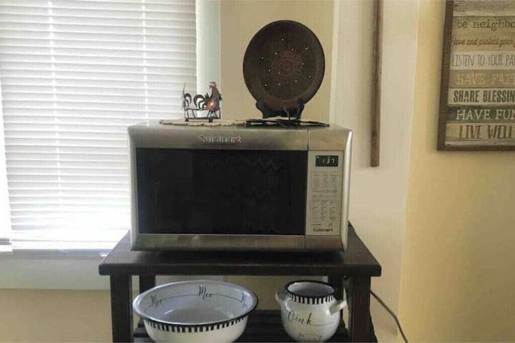 A kitchen with a microwave on a stand, a bowl, and a mug on the counter.