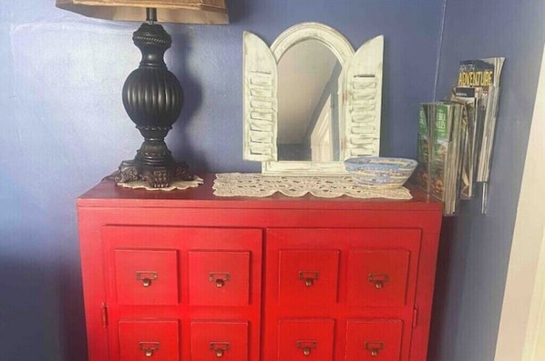 Un aparador rojo con varios cajones, un espejo con un copo de encaje y una lámpara.
