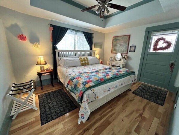 Une chambre à coucher comprenant un lit, une table de chevet, une commode, un ventilateur de plafond et une porte décorée d’une guirlande.
