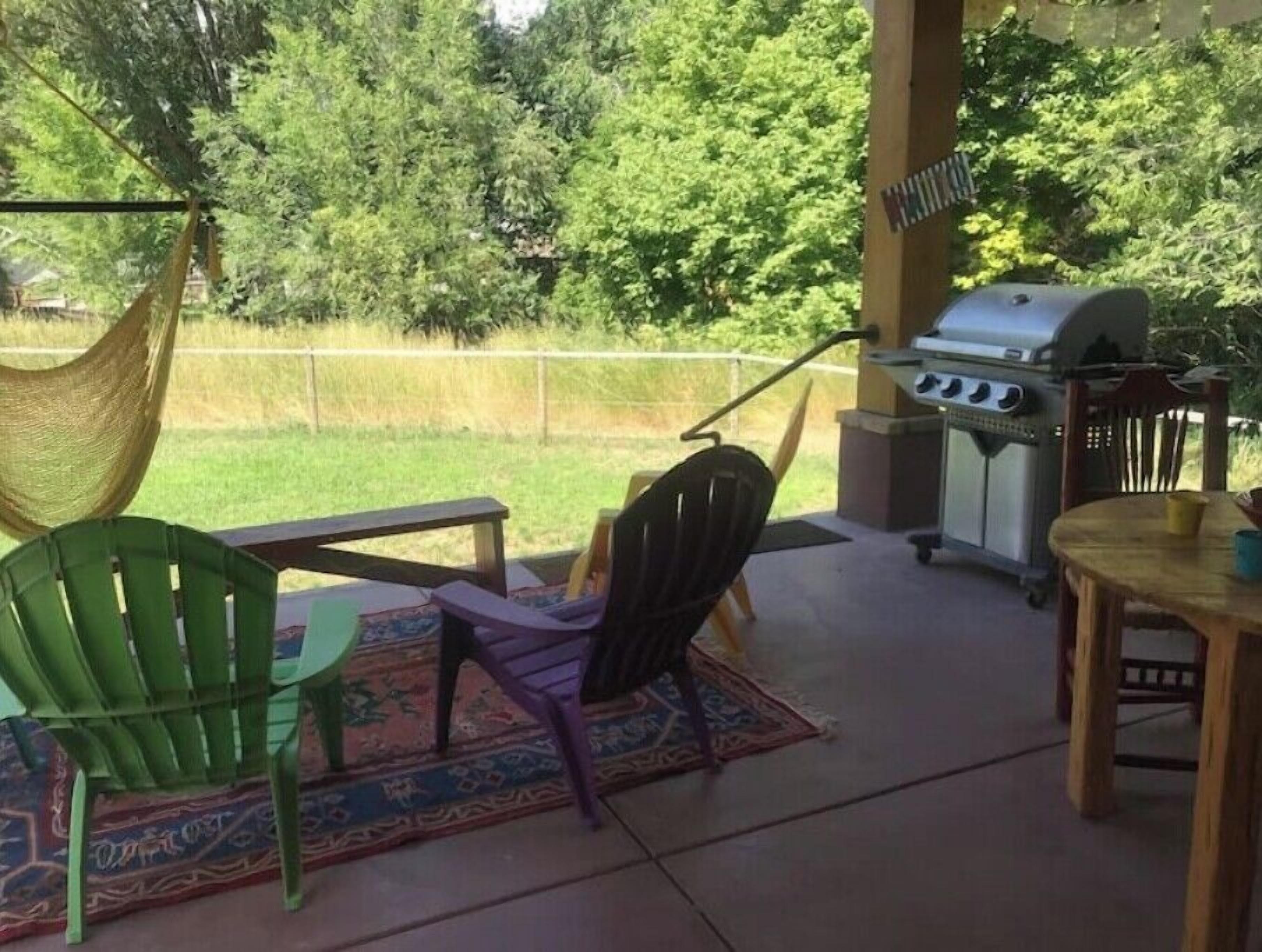 Un patio al aire libre con una hamaca, una parrilla y una mesa con sillas.