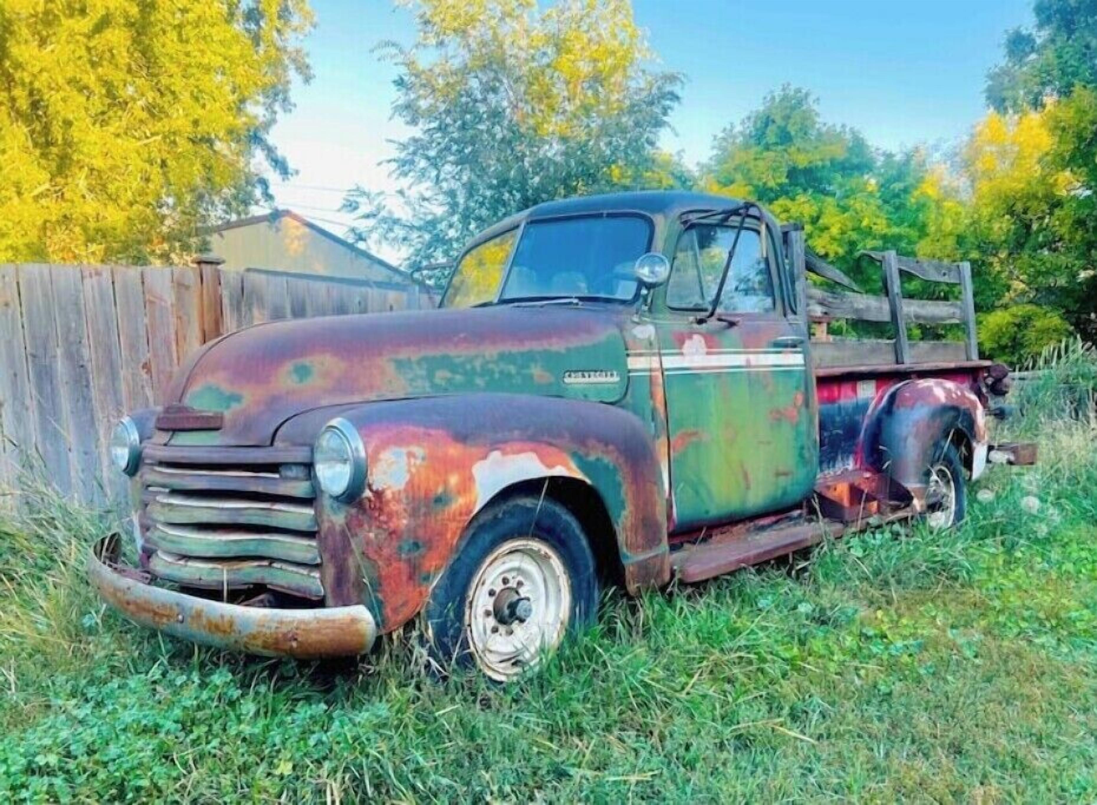 Un vieux camion-benne rouillé est garé dans un espace herbeux, avec une clôture en bois et des arbres en arrière-plan.