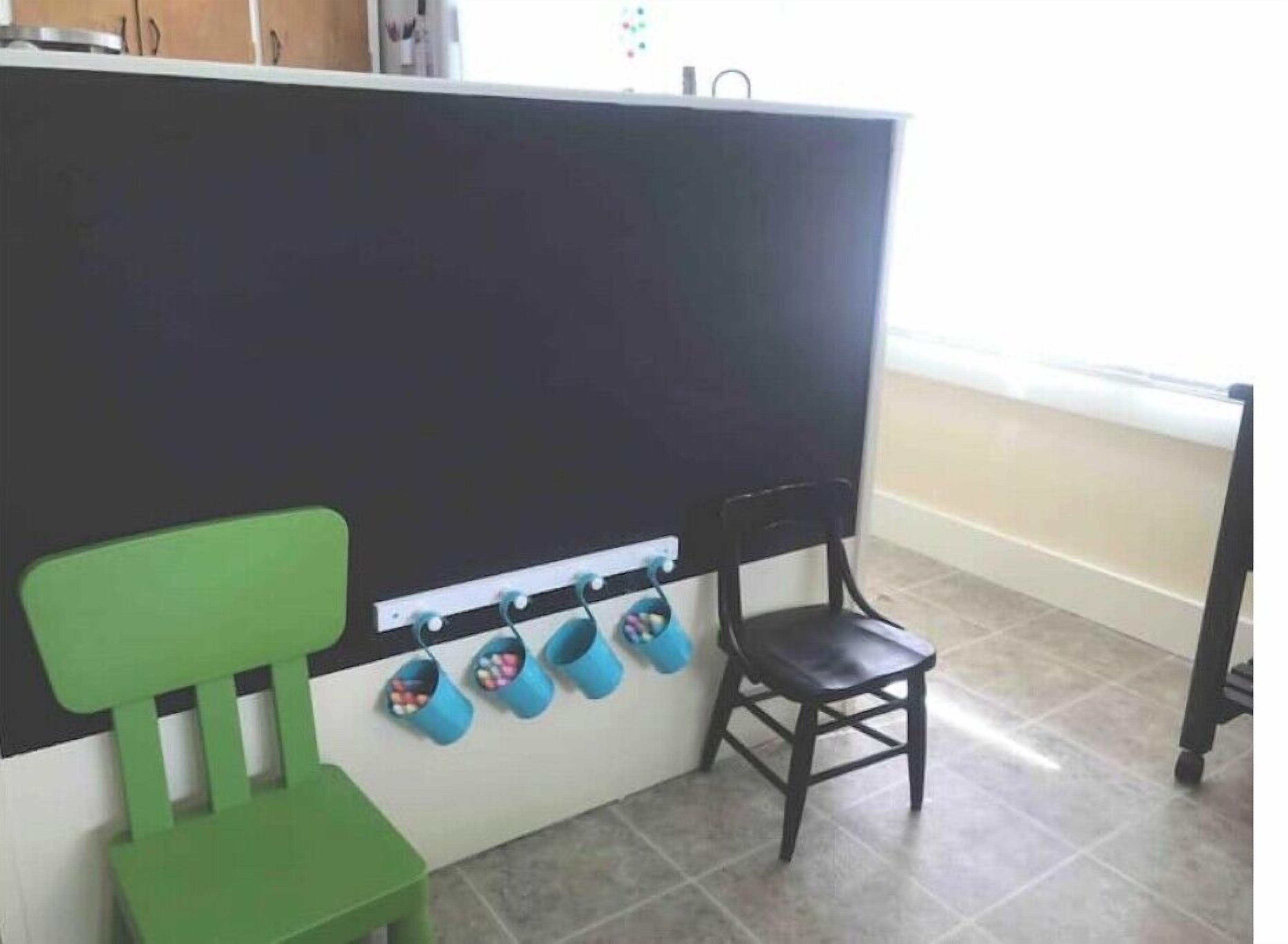 Una habitación con un separador negro, una silla verde, una silla de madera y una fila de pantuflas azules colgadas en ganchos.