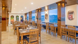 A restaurant with wooden furniture, large windows, and a view of the mountains. - Manaw Valley Resort (Shimla)