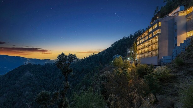 A modern building with multiple floors, surrounded by a forested hillside. - Manaw Valley Resort (Shimla)
