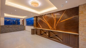 A modern reception area with a wooden accent wall, a stone accent wall, and a blue window view. - Manaw Valley Resort (Shimla)