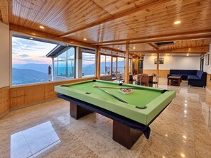 Una mesa de billar en una habitación con techo de madera y ventanas amplias.