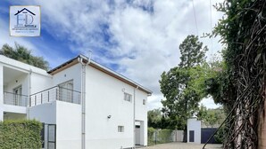 Une cour avec un chemin pavé, des bâtiments blancs et un arbre.