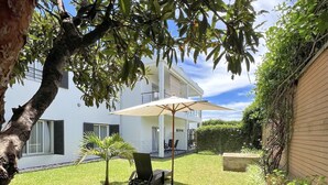 A modern two-story house with a well-maintained lawn, a lounge chair, and a patio umbrella. - E&D  Apartment With Private Garden, Quiet and Secure Ideal For Families (Antananarivo)