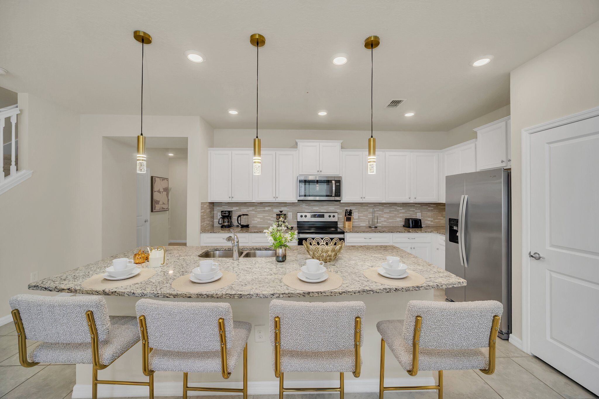 A modern kitchen with white cabinets, a granite countertop, stainless steel appliances, and a central island with bar stools.