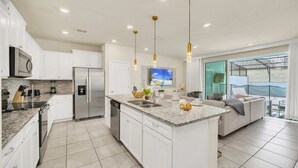 Una cocina moderna con armarios blancos, electrodomésticos de acero inoxidable, encimeras de granito e iluminación colgante.