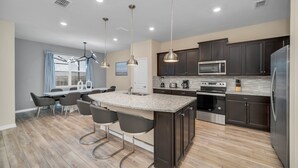 Une cuisine moderne avec des meubles de couleur sombre, des appareils en acier inoxydable et un îlot central doté de tabourets de bar.