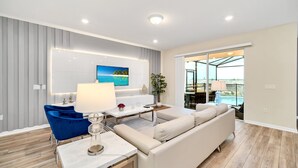 Un salon moderne avec un canapé, une table basse et un téléviseur. Il y a également un coin repas avec une table et des chaises. La pièce est dotée d’un parquet et d’une grande fenêtre.