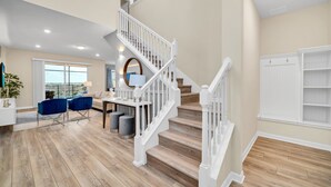 Un vaste espace de vie agrémenté d’un escalier en bois, d’une table à manger avec des chaises et offrant une vue dégagée grâce à une grande fenêtre.