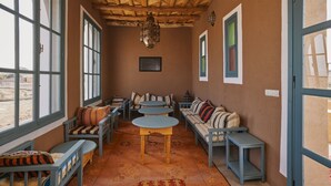 A cozy room with a wooden ceiling, large windows, a sofa set, and a small table. - Agafay Desert Hotel (Agafay)