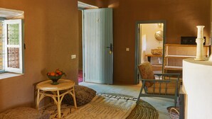 A cozy room with a wicker chair, a small table with a bowl of fruit, a blue door, and a patterned rug. - Agafay Desert Hotel (Agafay)