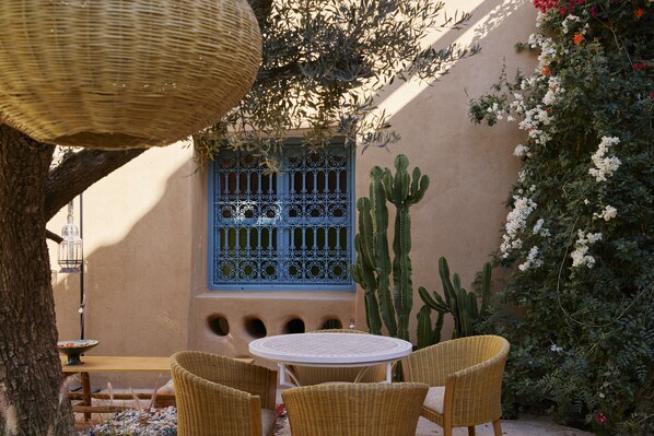A courtyard with a round table and wicker chairs, a blue window with decorative metal bars, and cacti. - Agafay Desert Hotel (Agafay)