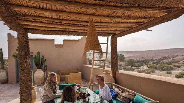 A terrace with a thatched roof, cacti, and a view of a desert landscape. - Agafay Desert Hotel (Agafay)