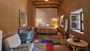 A bedroom with a bed, dresser, and chair, a window with a view, and a decorative ceiling light. - Agafay Desert Hotel (Agafay)