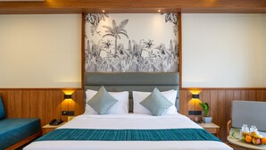 Habitación de hotel con una cama grande, dos mesitas de noche, una silla, una pequeña mesa con fruta y un mural en la pared.