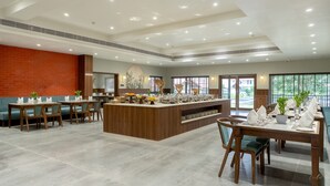 Un comedor amplio con un bufé central, diversas opciones de distribución de mesas y grandes ventanales que aportan luz natural.