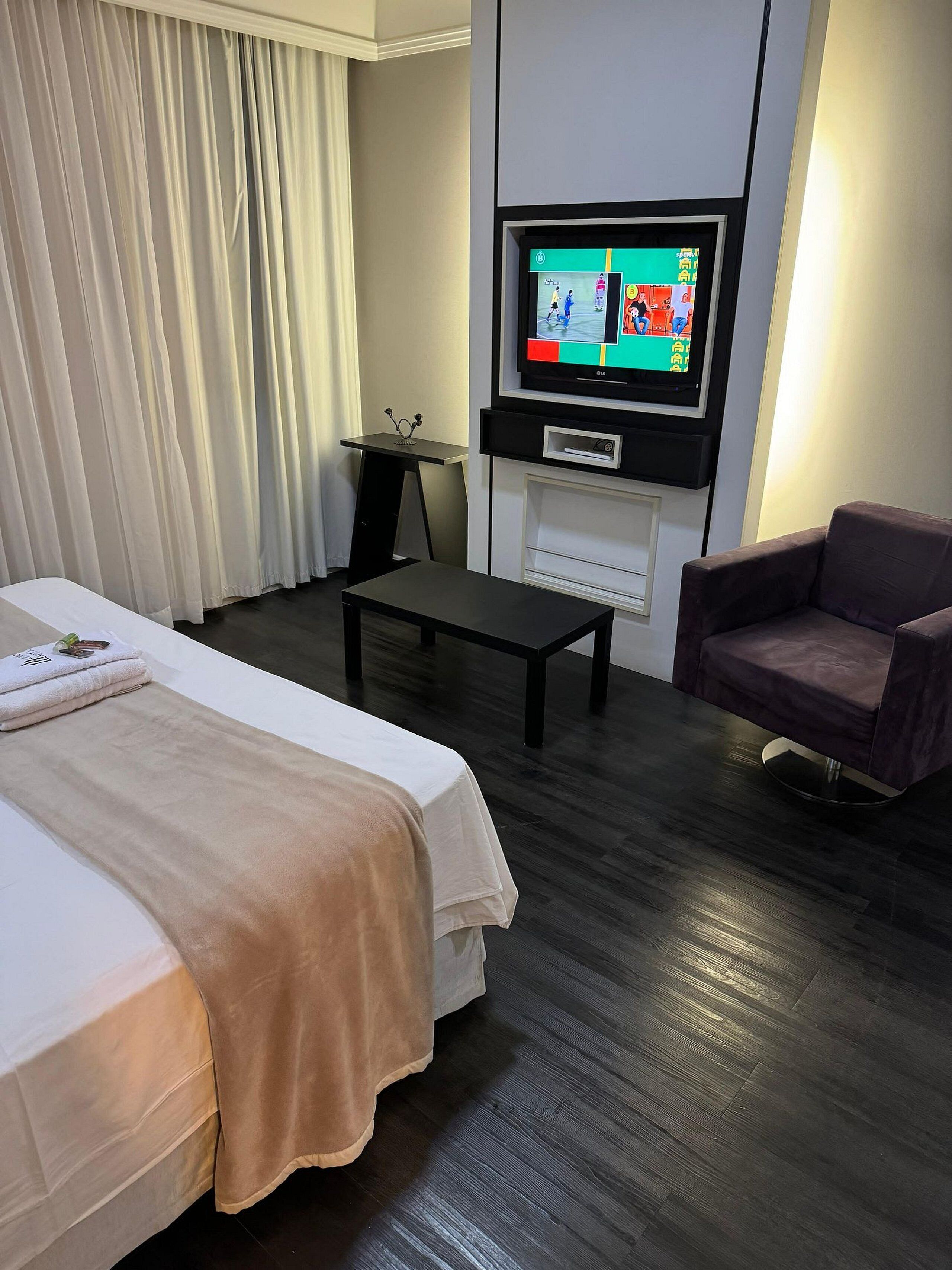 Habitación de hotel con dos camas, un televisor montado en la pared, una mesita y una silla.