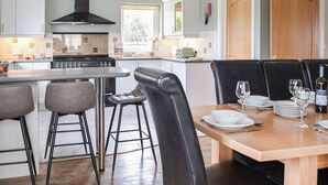 A modern kitchen with a central island, bar stools, and a dining table set for six. - A spacious holiday home with a heavenly hot tub close to stunning beaches. (Llechryd, near Cardigan)