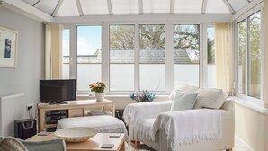 A bright, sunlit room with a large window, a television, a sofa, and a coffee table. - A spacious holiday home with a heavenly hot tub close to stunning beaches. (Llechryd, near Cardigan)