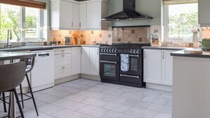 A modern kitchen with white cabinets, a black stove, and a window with a view of greenery. - A spacious holiday home with a heavenly hot tub close to stunning beaches. (Llechryd, near Cardigan)