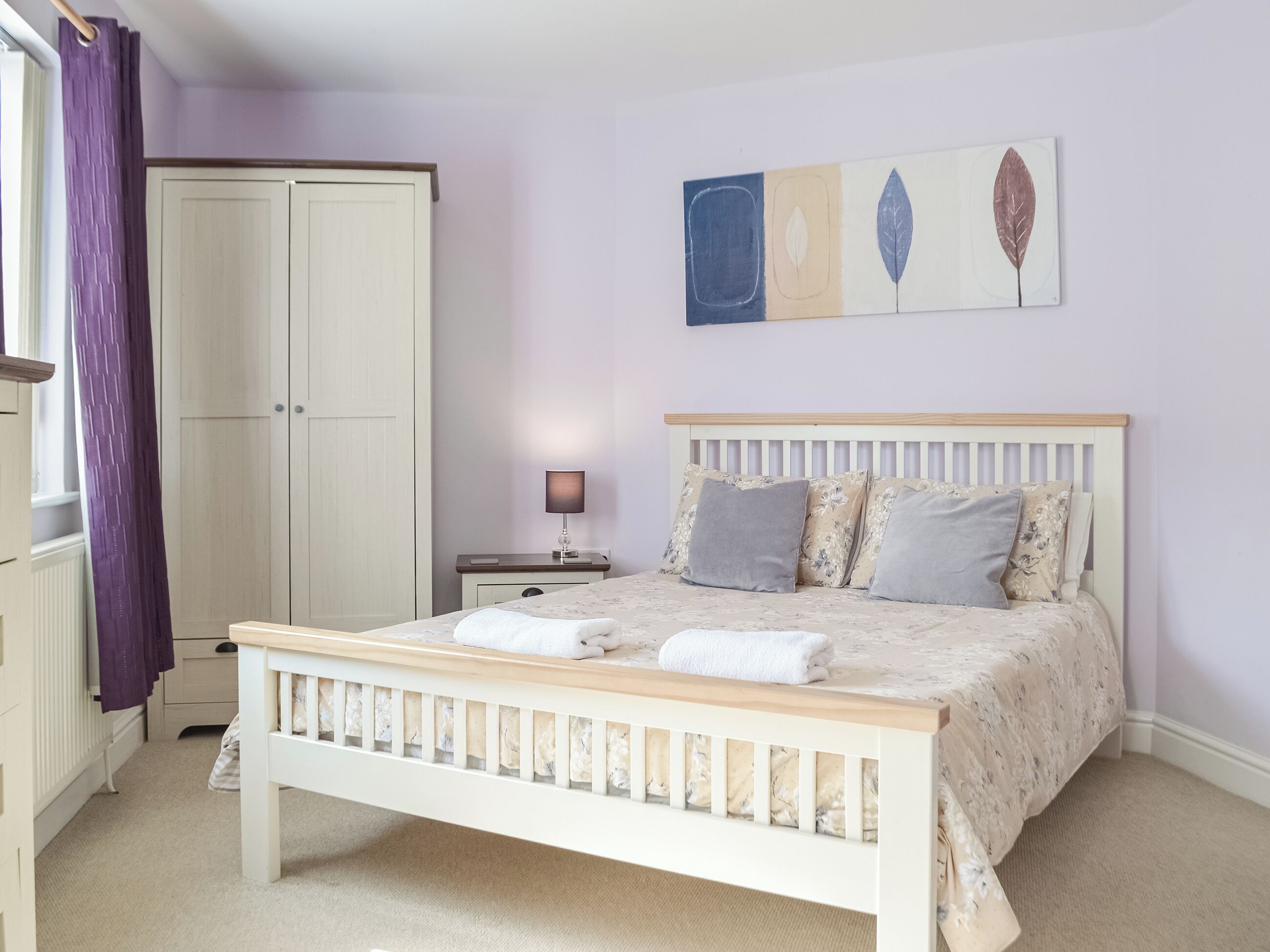 A bedroom with a bed, bedside table, lamp, and a wardrobe.
