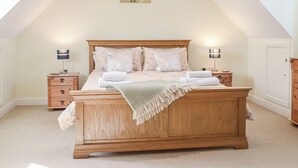 A bedroom with a wooden bed, two bedside tables, a nightstand, and a painting on the wall. - A spacious holiday home with a heavenly hot tub close to stunning beaches. (Llechryd, near Cardigan)