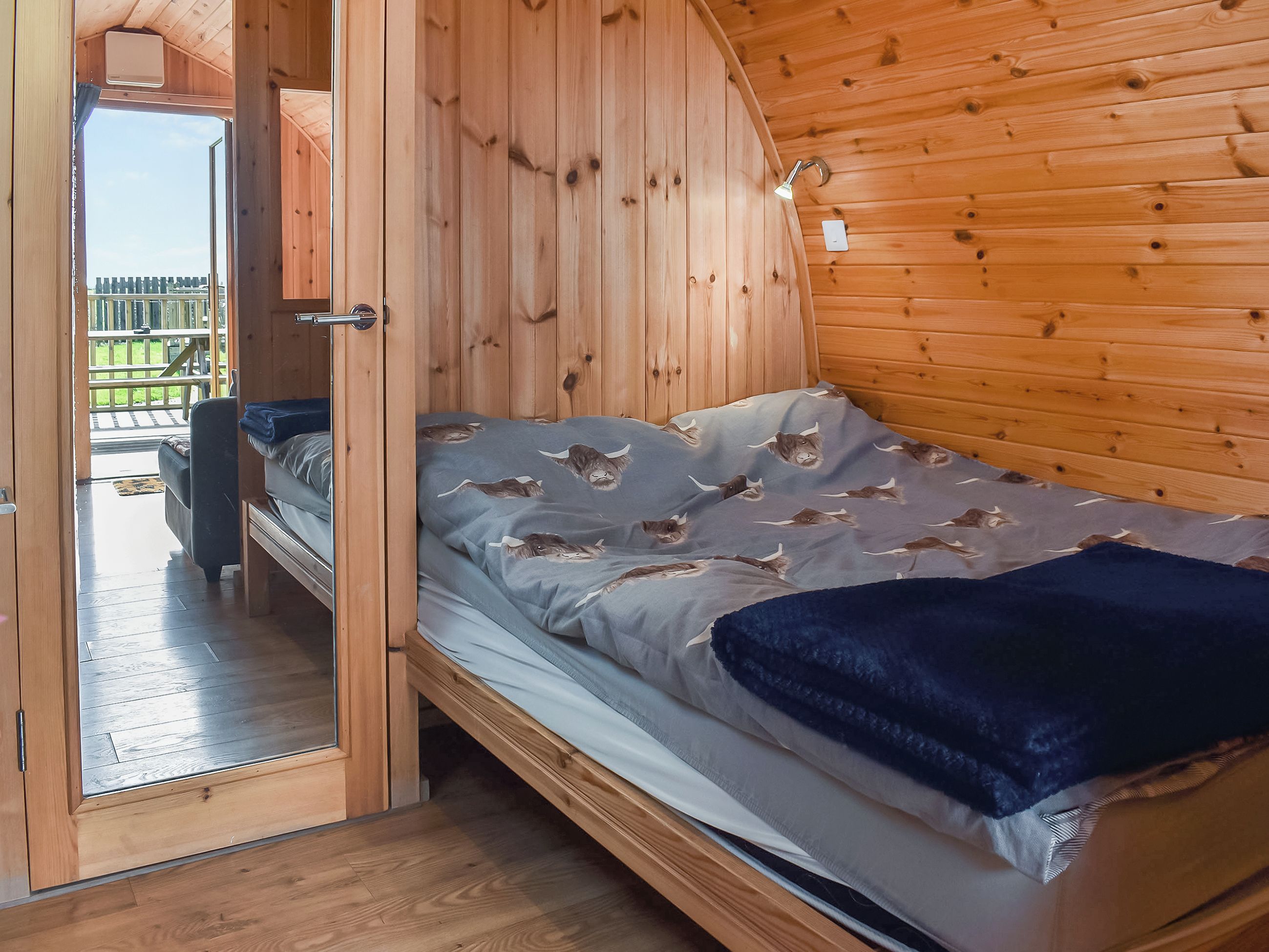 Una cabaña de madera con una cama que tiene un edredón gris con estampados de animales, techo de madera y vistas a una terraza exterior.