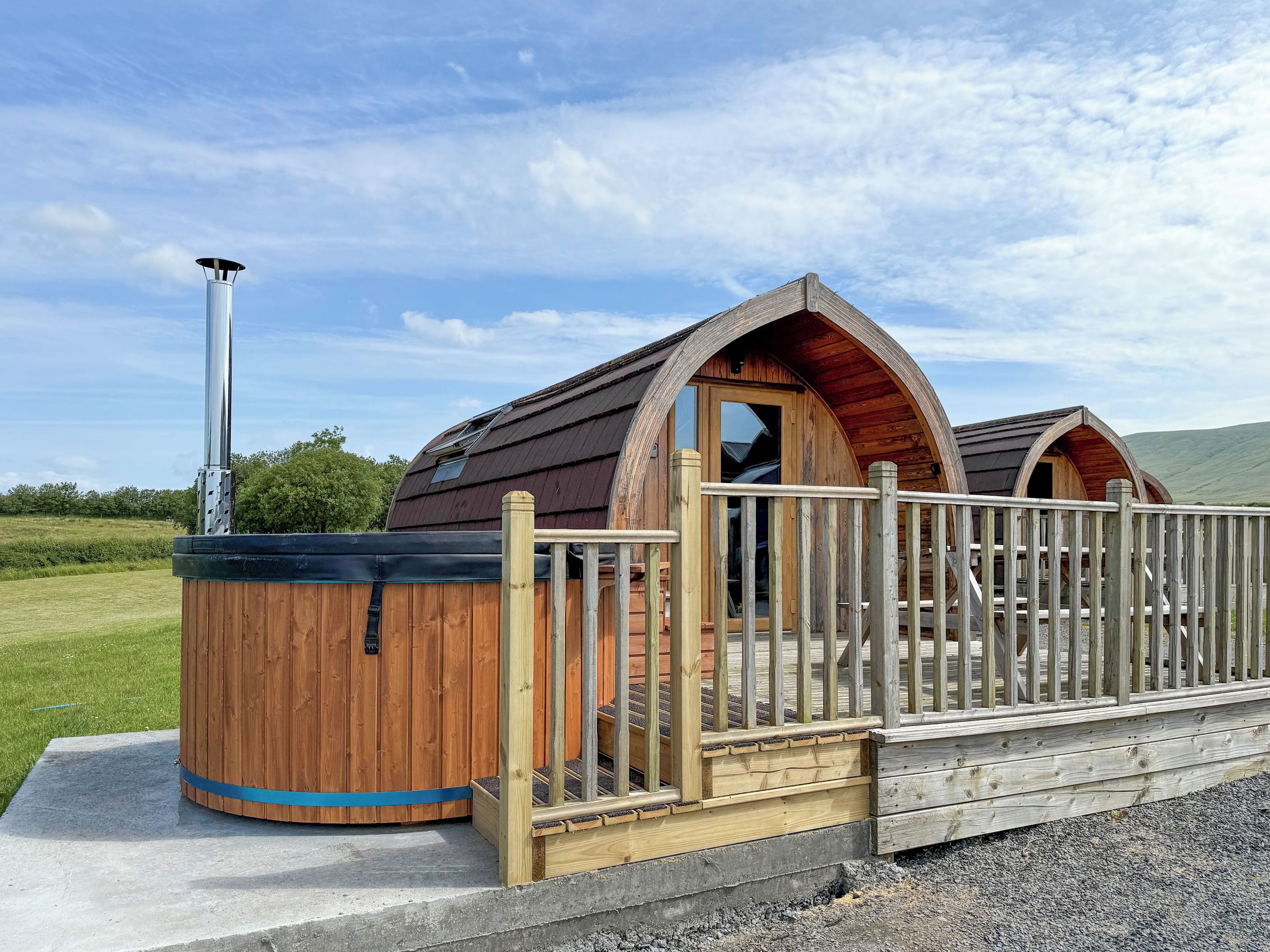 Una cabaña de madera con jacuzzi, terraza de madera y chimenea de metal.
