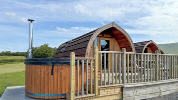 Una cabaña de madera con jacuzzi, terraza de madera y chimenea de metal.