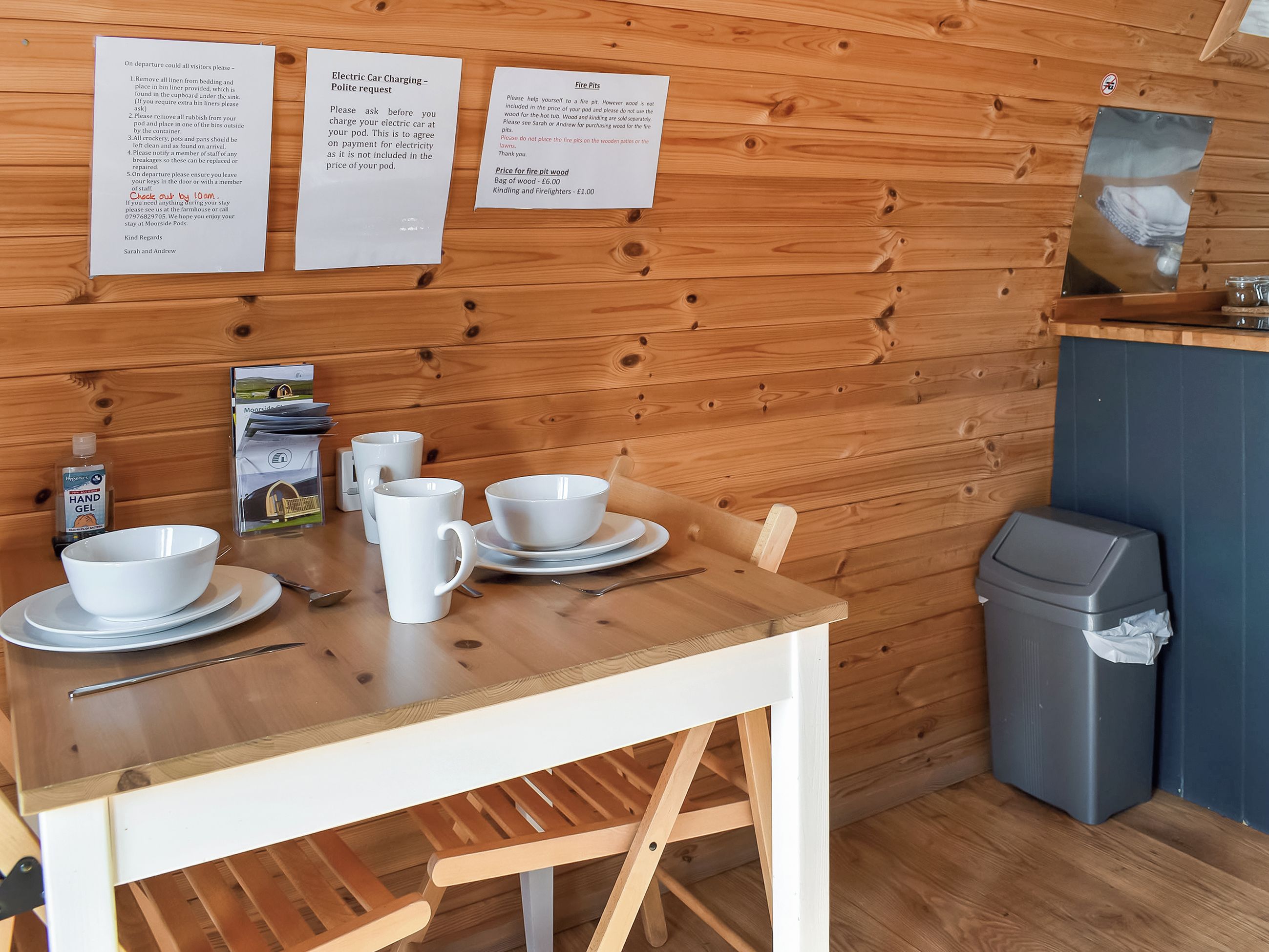 Un interior de madera con una mesa lista para comer, un cubo de basura y carteles informativos en la pared.