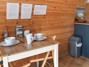 A wooden interior with a table set for dining, a trash bin, and informational signs on the wall.