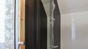 A modern bathroom with a glass shower enclosure, a wooden door, and a white tiled wall. - 1 bedroom accommodation in Corney, near Millom (Corney, near Millom)