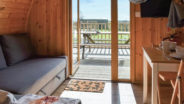 En træhytte med sofa, spisebord og udsigt til en terrasse og udendørs område.
