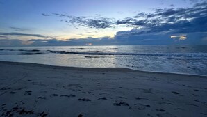 A beach with footprints leading to the water, a clear sky, and the sun setting or rising. - Mermaids' BeachHouse: Walk2Beach • Pool • KingBed (Cocoa Beach)